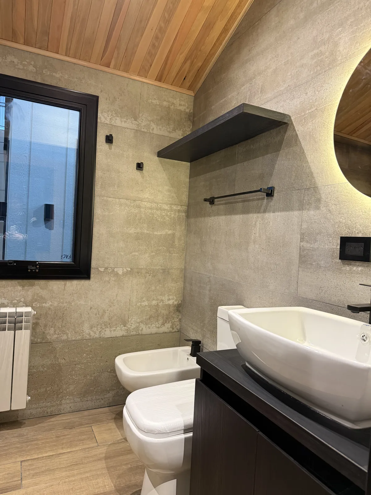 Baño con vanitory negro, bacha de apoyo y revestimiento símil cemento casa modular Faci House