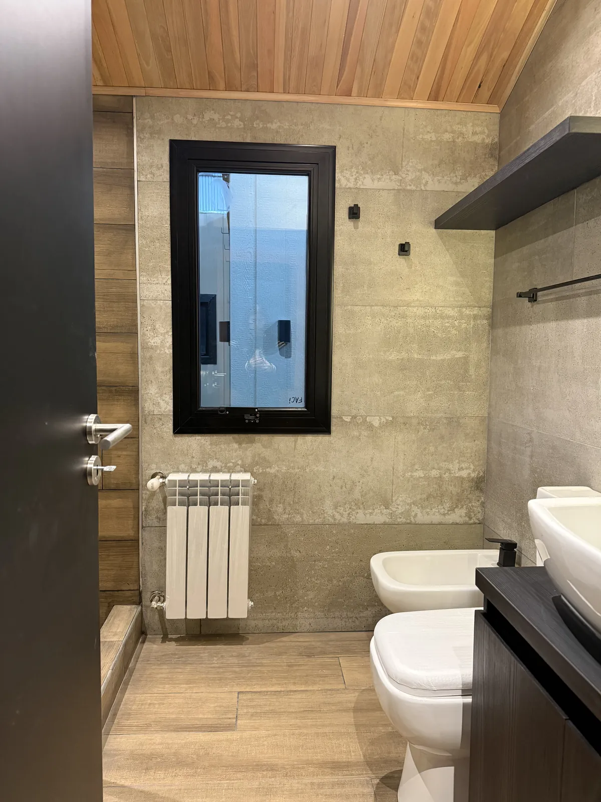 Baño con ventana, radiador y revestimiento símil cemento casa modular Faci House