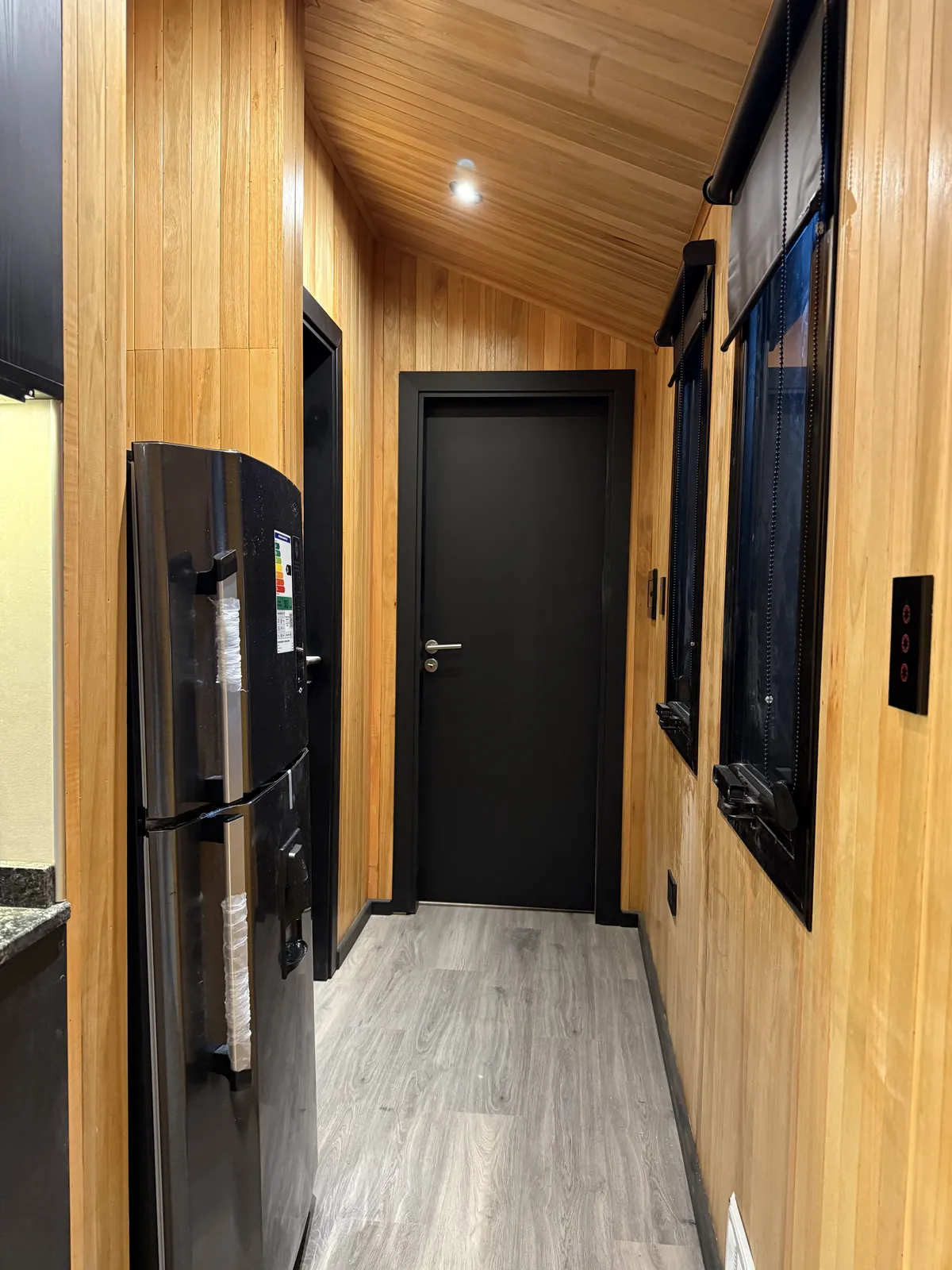 Pasillo con revestimiento de madera y carpintería negra casa modular Faci House